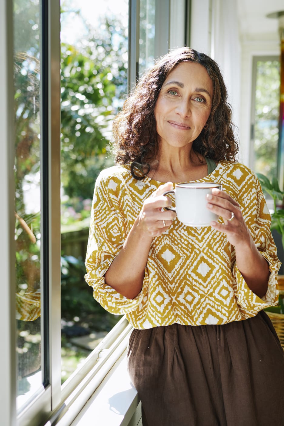 Jill holding a mug beside a sunlit window